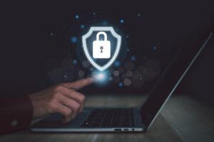 Hand using a laptop while touching a digital security shield with a padlock icon representing cybersecurity and antivirus protection.
